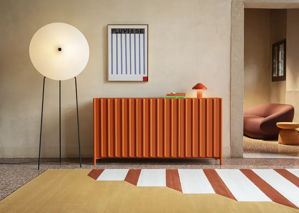 Ingresso con credenza arancione a doghe verticali, lampada da terra sferica, quadro astratto e tappeto geometrico bicolore