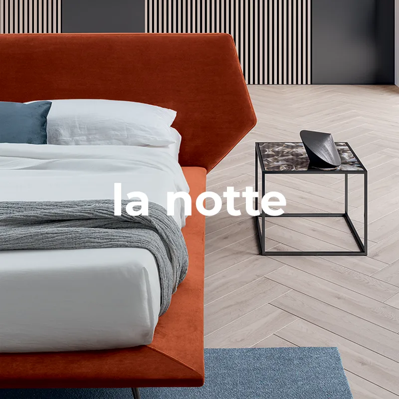 Dettaglio letto matrimoniale con testiera in velluto rosso, biancheria chiara e comodino in metallo nero con piano in marmo