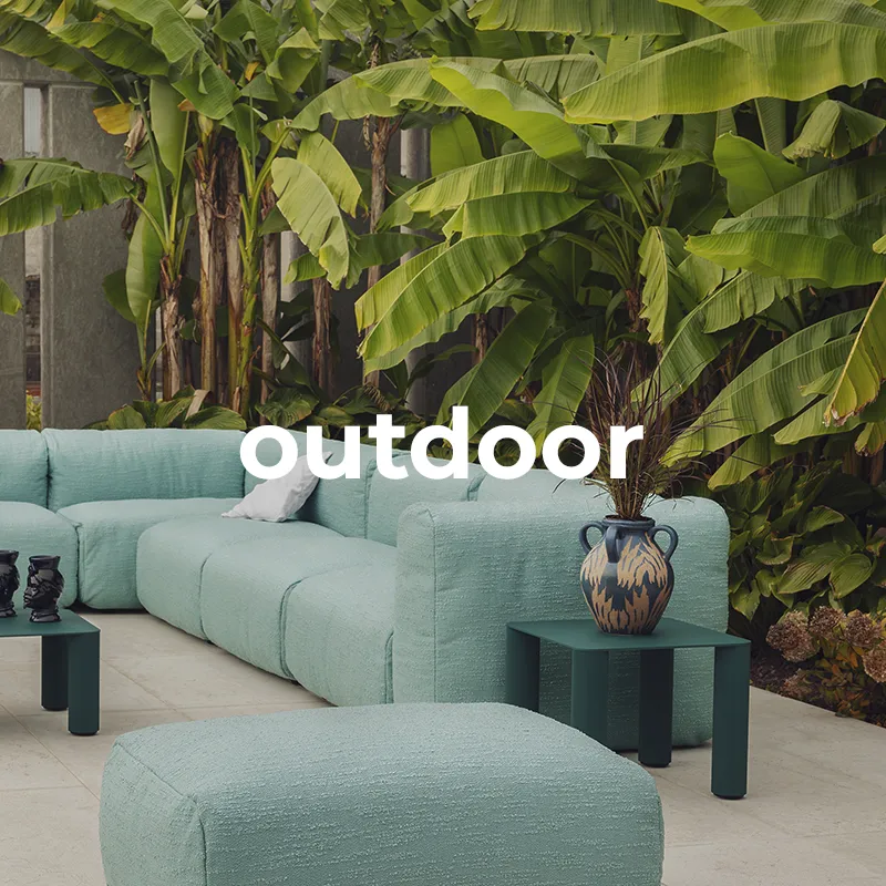 Salotto da esterno con divano modulare e pouf in tessuto verde acqua, tavolini coordinati e vegetazione tropicale