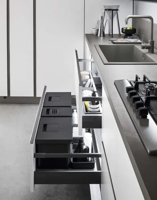 Dettaglio cassetti estraibili cucina con sistema di organizzazione interna in grigio scuro e piano di lavoro con fuochi a gas