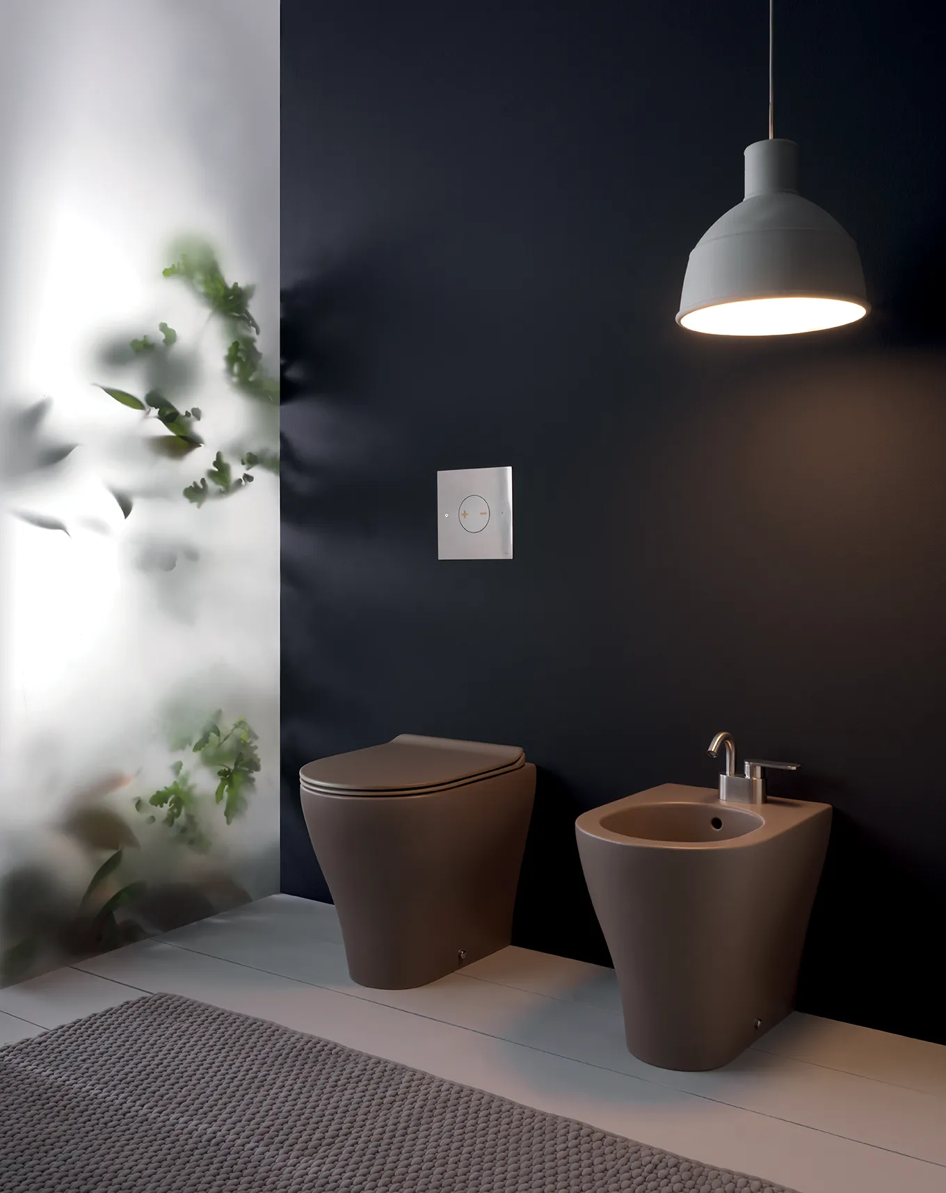 Sanitari a terra in ceramica color tortora opaco con placca di scarico cromata su parete scura