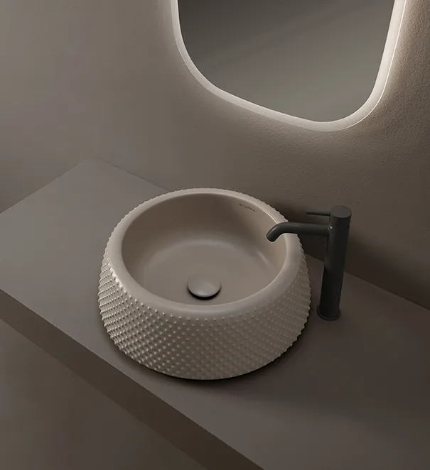 Lavabo d'appoggio rotondo con superficie a rilievo puntinato, rubinetto nero e specchio retroilluminato con bordi arrotondati